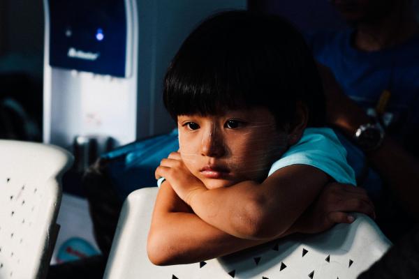 A little Asian girl has her chin on top of her crossed arms, and is looking sad